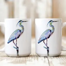 The Ship's Hold Watercolor Artwork 15oz Ceramic Mug, Heron on Branch (pair on table)